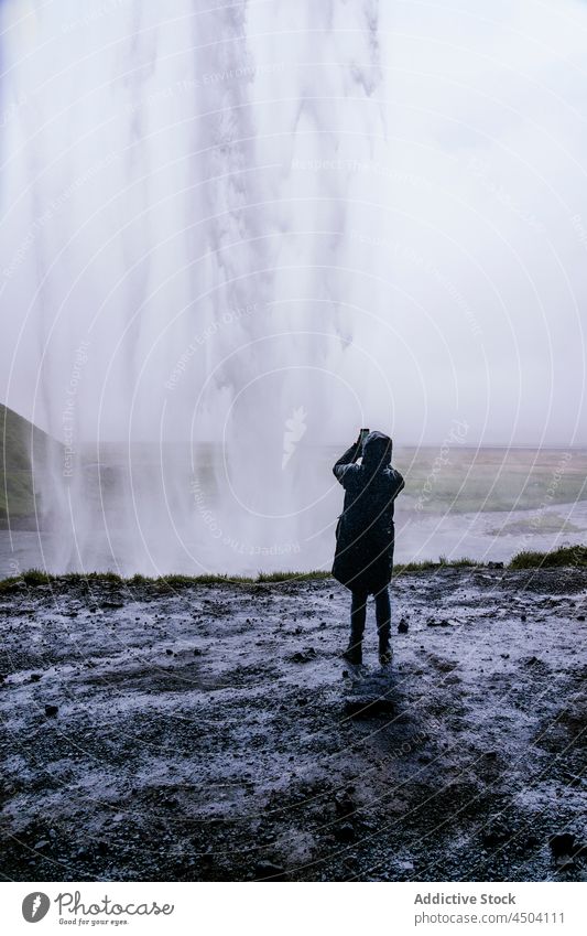 Anonymous tourist taking photo of amazing waterfall on smartphone on cloudy day person take photo nature trip explore traveler tourism landscape photographer