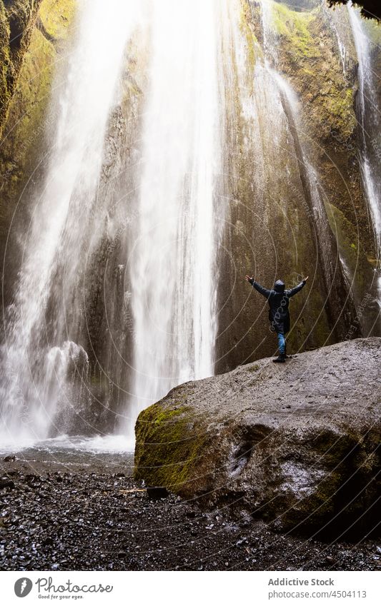 Anonymous traveler enjoying energy of powerful waterfall in rocky ravine person nature tourist outstretch admire canyon picturesque landscape cliff trip