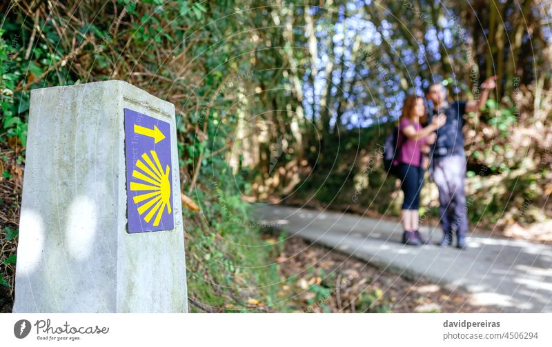 Signpost of Saint James way with pilgrims pointing saint james way milestone signpost copy space unrecognizable man woman couple hiker walk hiking stick shell