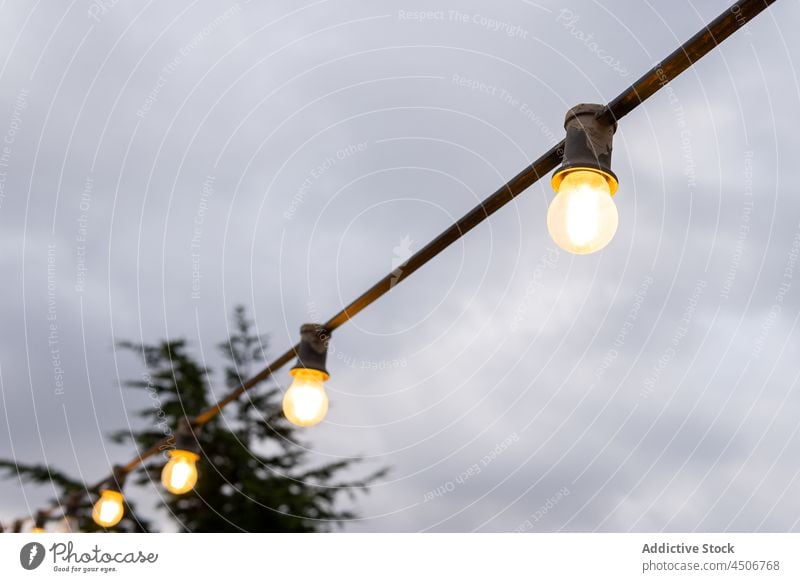 Hanging light bulbs under a cloudy sky electric line outdoor electricity lamp party hanging wire dusk grey group illuminated lightbulb silhouette copy space