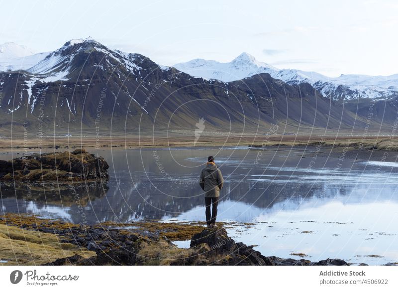 Anonymous male traveler admiring mountainous lake against blue sky man admire scenic landscape highland range nature recreation reflection snow casual alone