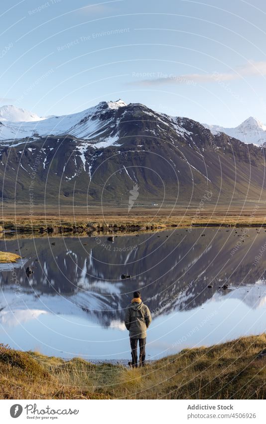 Anonymous male traveler admiring mountainous lake against blue sky man admire scenic landscape highland range nature recreation reflection snow casual alone