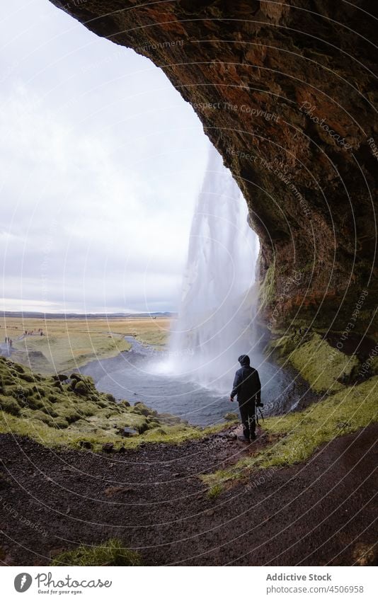 Unrecognizable man standing near rapid waterfall flowing through rocky cliff cave admire nature power traveler explore landscape tourist stream wanderlust male