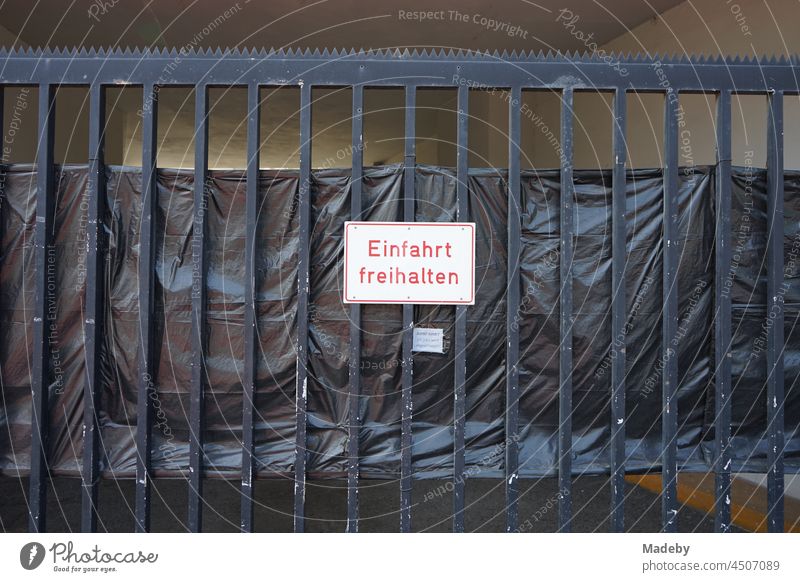 Keep driveway free sign in red on white at a black steel gate with privacy screen made of black plastic foil in the north end of Frankfurt am Main in Hesse, Germany