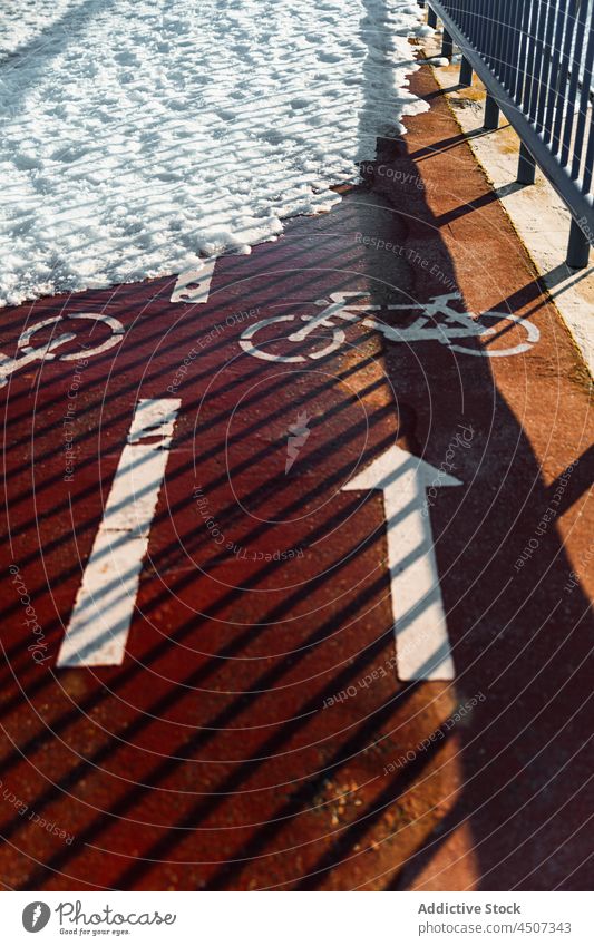 Bicycle lane on snowy fenced road bicycle path direction facility winter arrow way route bike paint street sunlight activity ground symbol urban line