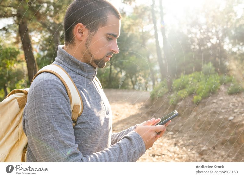 Serious ethnic guy using smartphone in forest man message nature concentrate tree mountain traveler trekking activity trip male young hispanic casual backpack