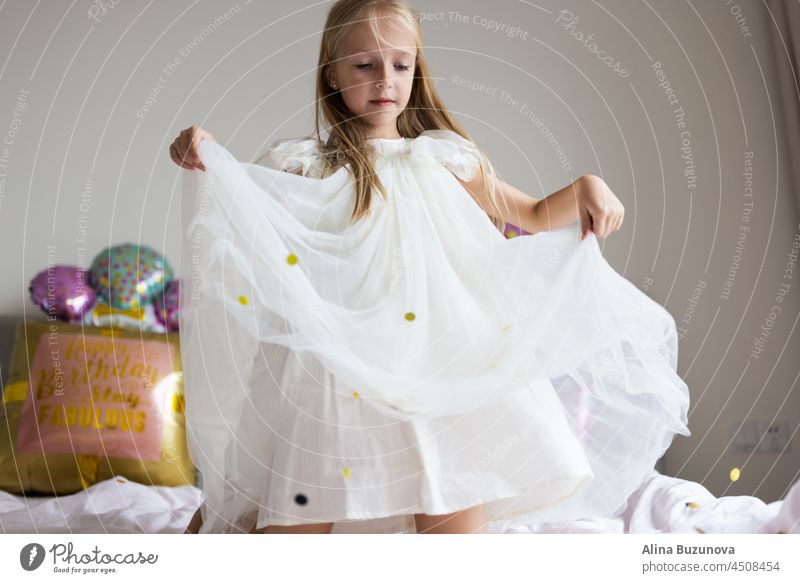 Cite little caucasian girl celebrating eight years old birthday at home. Stylish Kid wearing fashionable dress and having fun with confetti on bed Confetti