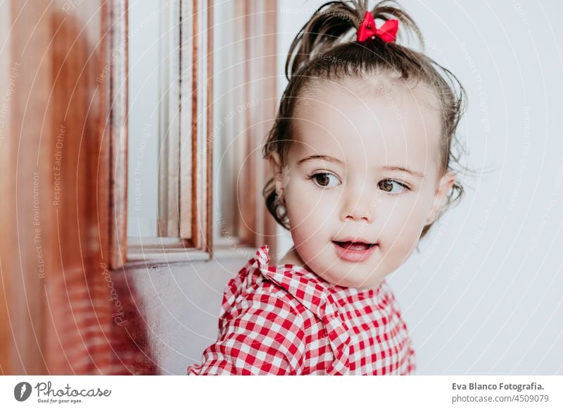 close up portrait of beautiful baby girl at home looking by window door. One year old girl. Lifestyles indoor caucasian waiting gorgeous smiling happy innocence