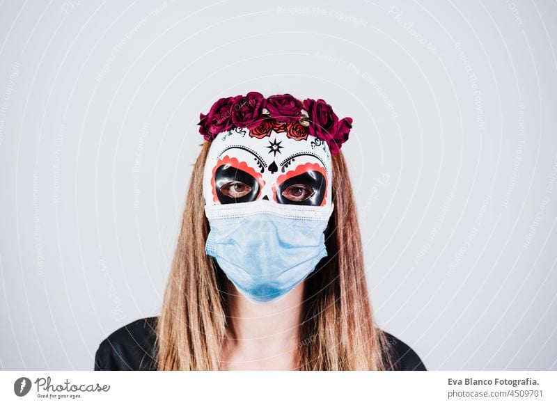 woman wearing mexican face mask during halloween celebration. skeleton costume and red roses diadem on head. woman wearing blue face mask during pandemic corona virus. Halloween party concept