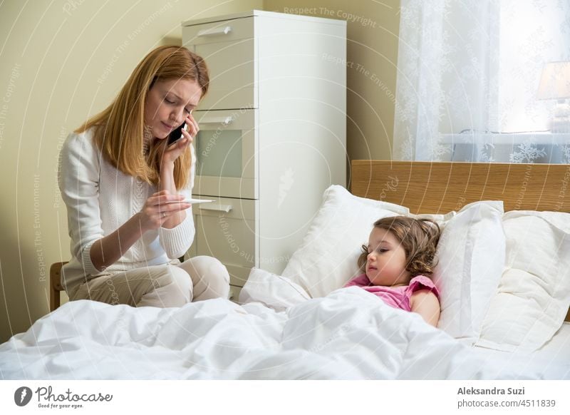 Mother taking temperature of her sick child. Sick child with high fever lying in bed and mother holding thermometer. Hand on the forehead. coronavirus Fever