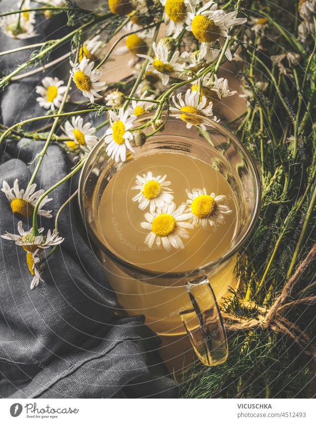 Close up of herbal tea with fresh chamomile in glass cup on kitchen table with dish towel. Front view. close up front view aroma aromatic beverage blossom