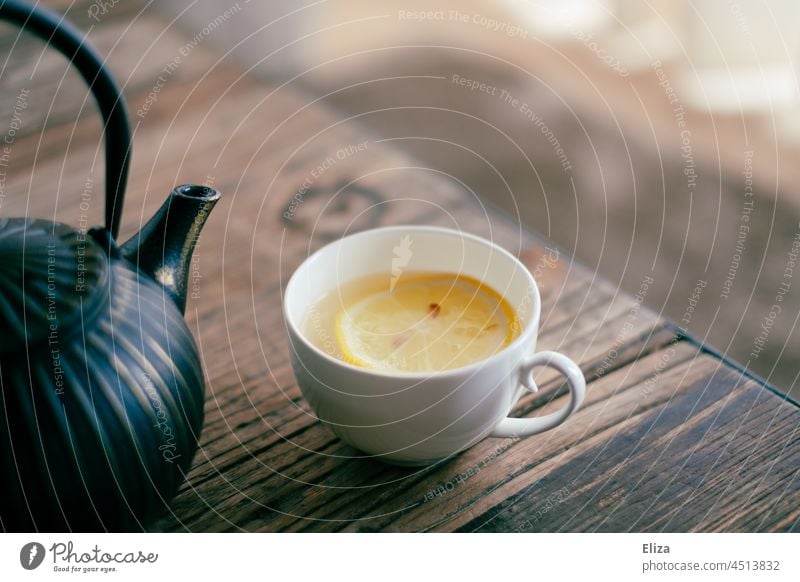 Teacup with tea and slice of lemon next to black teapot on a coffee table Tea cup Teapot Lemon Slice of lemon Hot drink Cup Table Black White Teatime Wood