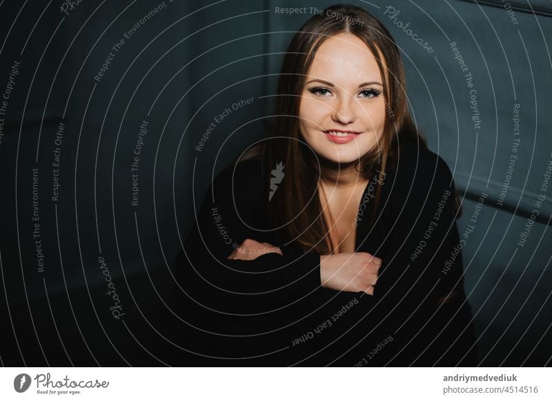 beautiful smiling girl in a black dress sitting on the background of a graphite wall woman hair smile happy light natural lens drawing shadow gray up glare