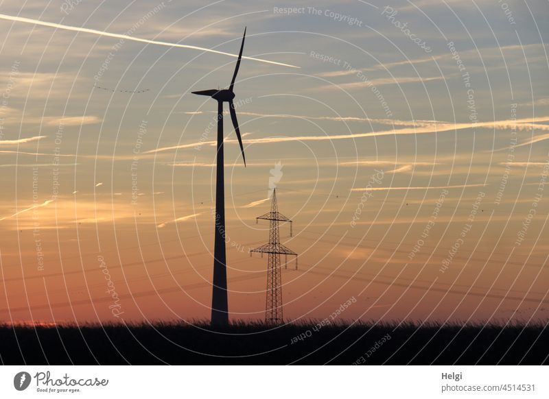 before sunrise - a windmill and a power pole are standing on a field , morning atmosphere in front of a reddish sky Pinwheel Wind energy plant Electricity pylon