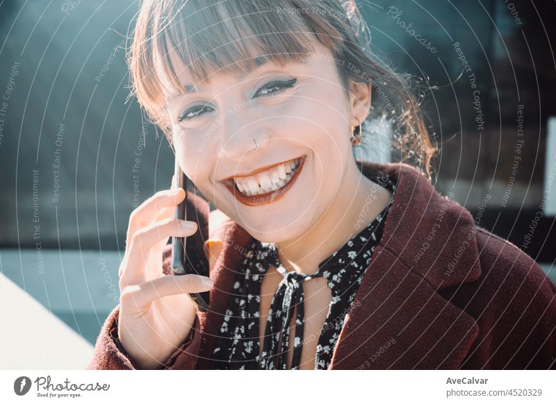 Young woman entrepreneur on a styled coat, smiling to camera while making a business call during a sunset, young business and future enterprise businesswoman