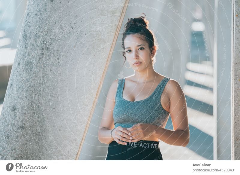 Young african woman looking to camera on sport clothes during a sunset in the city, concrete background, urban sport style, copy space, young athletics exercise