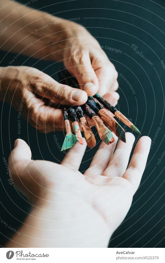 Old hands giving painting pencils brushes to another hand, black background, moody style. Artist style. art concept artist creativity inspiration paintbrush