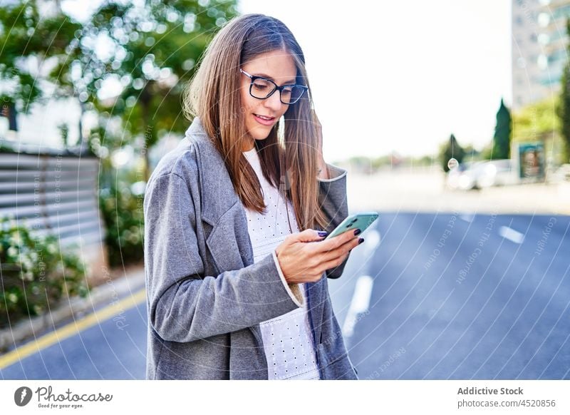 Smiling woman texting on smartphone while walking on sidewalk positive using message street formal connection internet city female work professional surfing