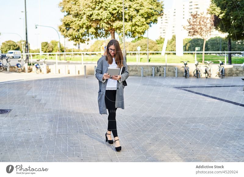 Focused businesswoman watching tablet on street entrepreneur using surfing online job busy female gadget eyeglasses device walking employee project manager