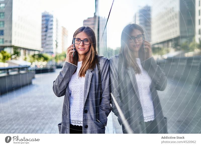 Smiling businesswoman talking on smartphone near building entrepreneur using phone call positive formal reflection conversation work female connection speak