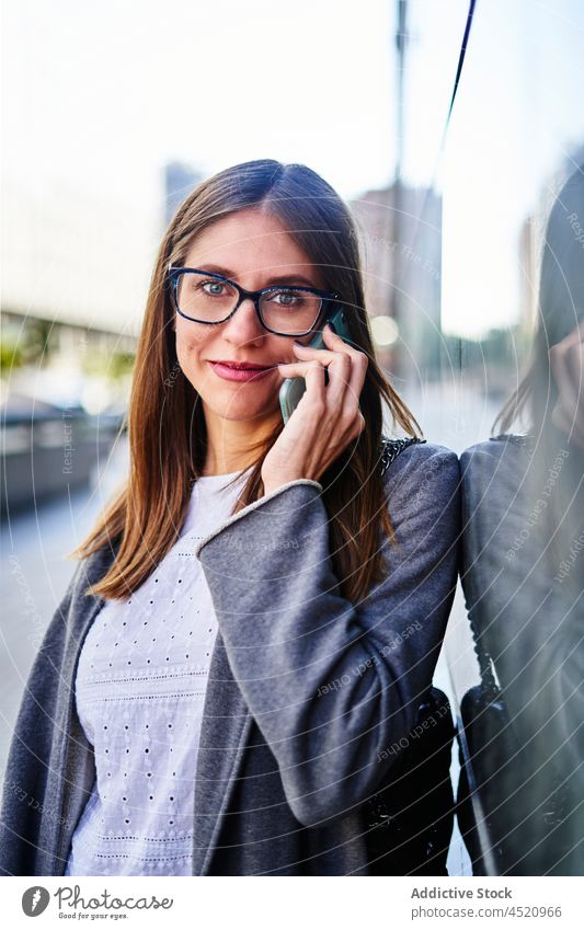 Smiling businesswoman talking on smartphone near building entrepreneur using phone call positive formal reflection conversation work female connection speak