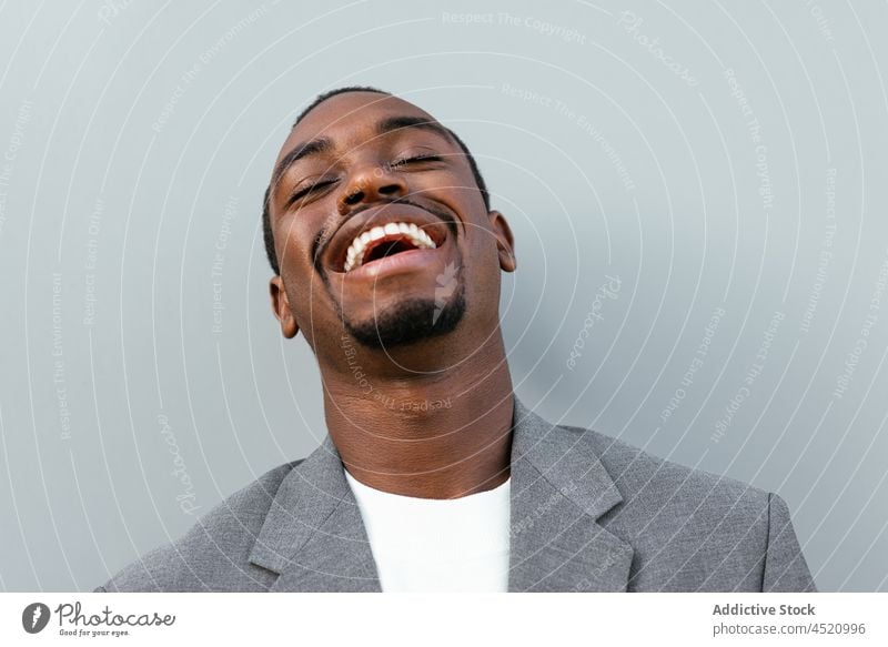 Positive black man in formal outfit standing near gray wall businessman positive elegant laugh respectable portrait professional appearance style well dressed