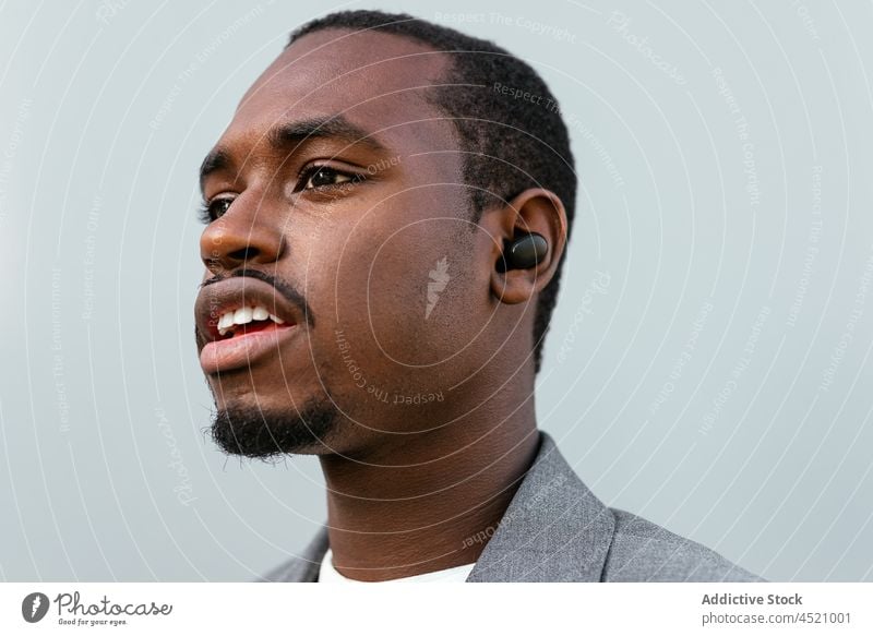 Positive black man in formal outfit standing near gray wall businessman positive elegant listen music earbuds respectable portrait professional appearance style