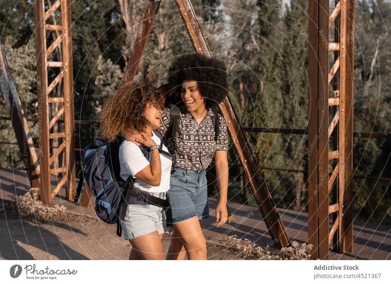 Black friends embracing on old bridge women laugh caress joy hug hike happy fun female cuddle best friend carefree adventure embrace backpack friendship