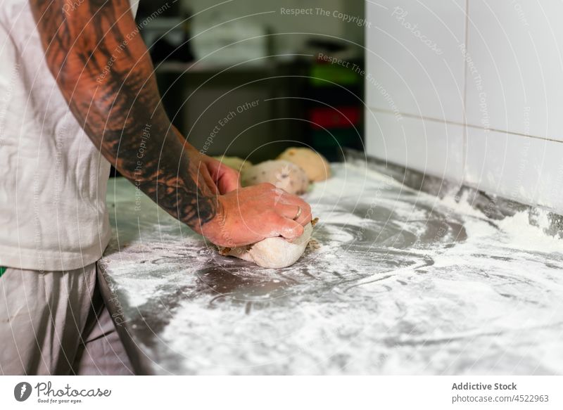 Young man rolling dough in bakehouse kitchen knead bakery bread prepare counter work pastry small business male young tattoo casual process flour ingredient