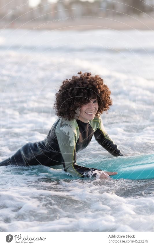 Smiling woman in wetsuit with surfboard in waving sea surfer wave enjoy beach relax foam coast female seawater splash curl afro seacoast summer chill sand