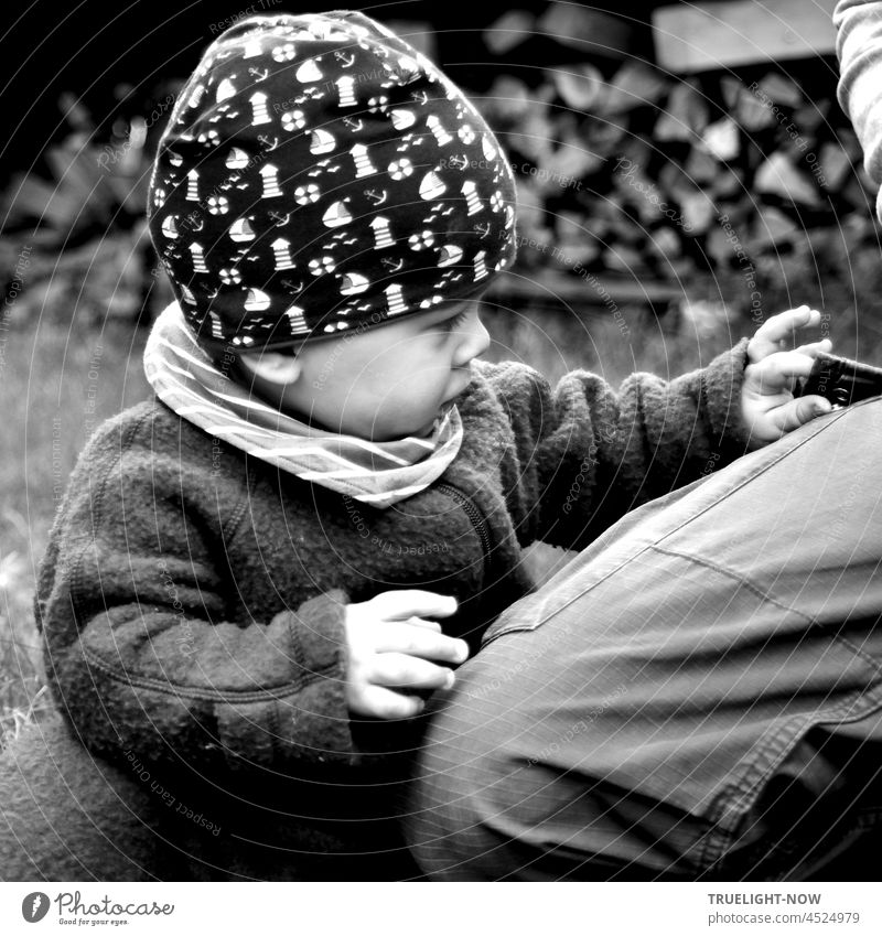 A little explorer, only 10 months old, seriously, highly concentrated and sensitively explores the mysterious pocket on his father's trousers with all his senses.