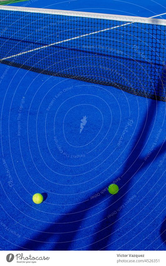 Two balls next to the serving lines of a blue paddle tennis court. shadows padel court courts padel tennis texture ground still life lawn artificial grass