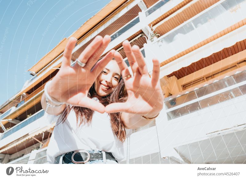 Close up portrait of young arab woman doing signs wearing white shirt and blue jeans smiling to camera on a block in the hood. Street life style, cool trendy. Social network concept