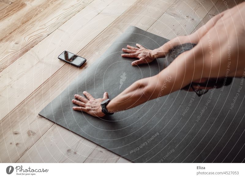 A man does yoga exercises on a yoga mat at home with a course on his phone Yoga Man Naked Lifestyle Cellphone Telephone Fitness wooden floor Black Yoga posture