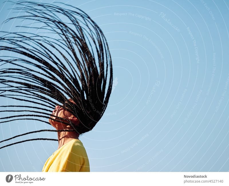 portrait of a young black girl with african braids flying, with copy space woman hair dreadlocks hairstyle yellow blue casual happy female outside outdoors