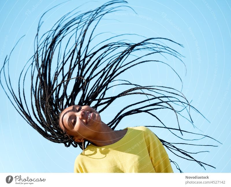 portrait of a young black woman with long hair, african braids or dreadlocks, isolated outdoors girl hairstyle copy space yellow blue casual happy female