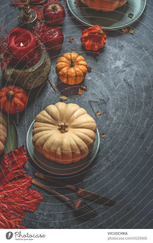 Autumn background with white pumpkin, plates, fall leaves and cutlery on dark concrete kitchen table. Rustic still life with kitchen utensils and seasonal decoration. Top view.