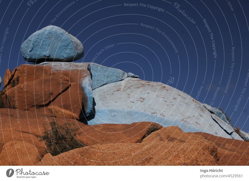 Roundish rocks in front of a dark blue sky. The upper part of the rocks is painted light blue, the lower part brown and natural. Art in the landscape. Blue Sky