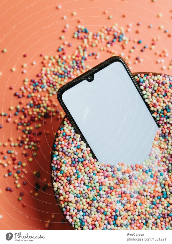 Fancy colorful image of a mobile phone in a bowl of colorful balls with blank screen with copy space, kid image, party social network style cyberspace gadget