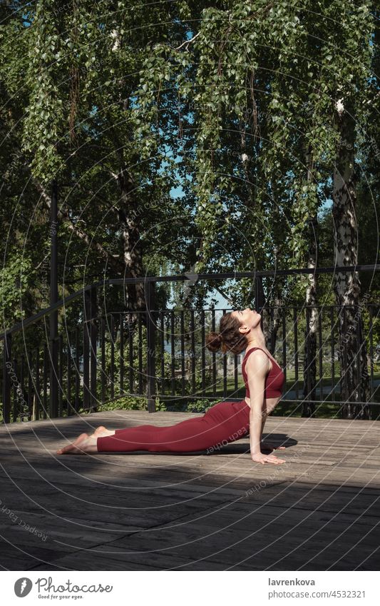 Young brunette woman practicing Upward-Facing Dog pose in the park on wooden platform wellness body Urdhva Mukha Svanasana sun salutation health lifestyle alone