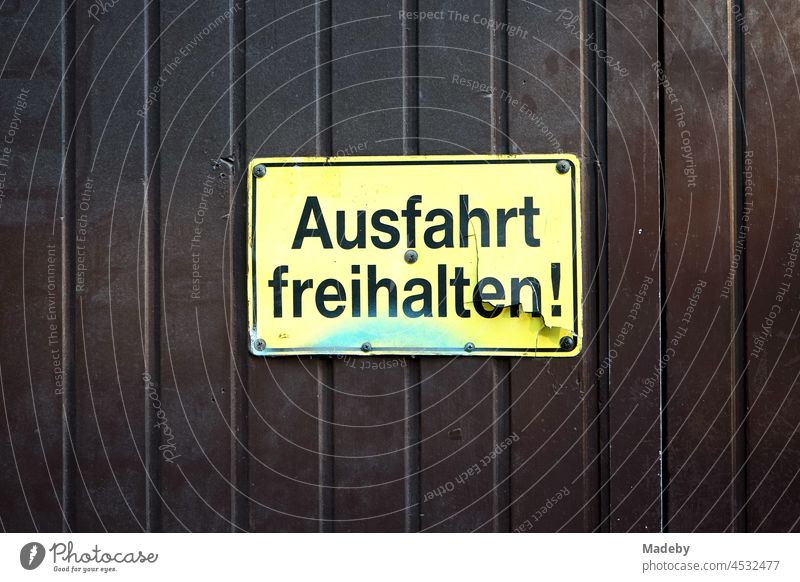 Broken yellow exit sign made of plastic with black writing on brown wooden gate in the north end of Frankfurt am Main in Hesse Highway ramp (exit) Yellow