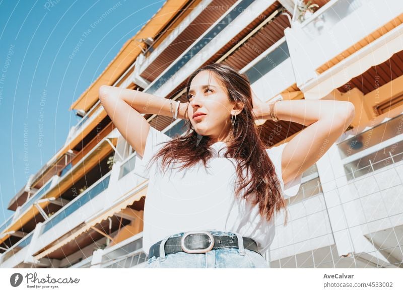 Close up portrait of young arab woman looking away from camera white shirt and blue jeans smiling to camera on a block in the hood. Street life style, cool trendy. Social network concept