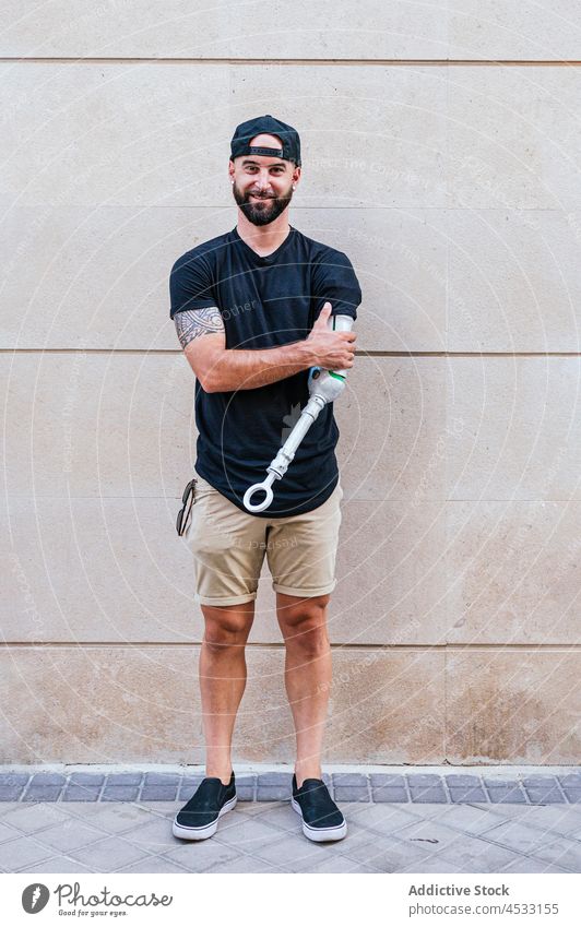 Smiling hipster with arm prosthesis in city man artificial limb bionic metal cool male content handicap wall lean street smile young beard style urban building