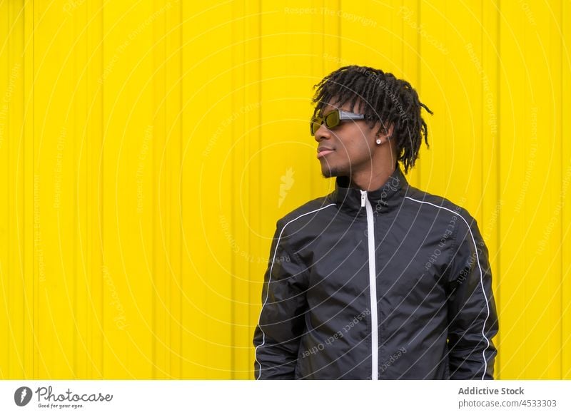 Smiling black man in sunglasses near yellow wall adjust cool street style positive bright trendy appearance accessory male dreadlocks carefree modern optimist