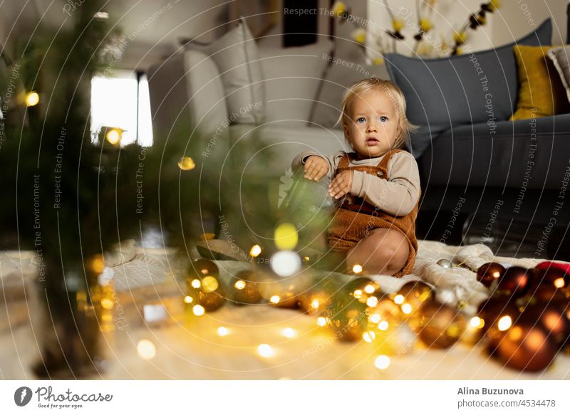 Lifestyle portrait of cute caucasian baby one year old playing with fir tree on floor at home. Merry Christmas xmas and happy new year 2022 christmas newborn