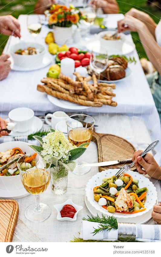 Family celebrations and food concept. The family is having dinner at a summer garden party. Table setting and decoration. Food and drinks. BBQ, vegetables, wine and other snacks. Life in the suburbs