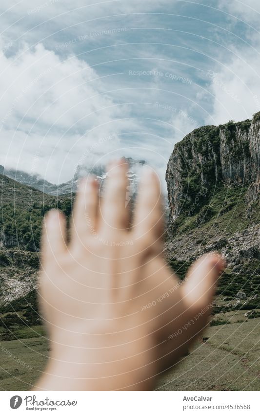 Moody wallpaper of an out of focus hand in front of a colorful landscape of the mountains of Asturias during a sunny day, Covadonga lakes, peaceful scenario, snowy mountains, copy space