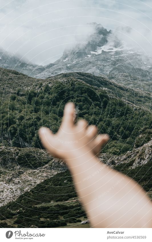 Moody wallpaper of an out of focus hand in front of a colorful landscape of the mountains of Asturias during a sunny day, Covadonga lakes, peaceful scenario, snowy mountains, copy space