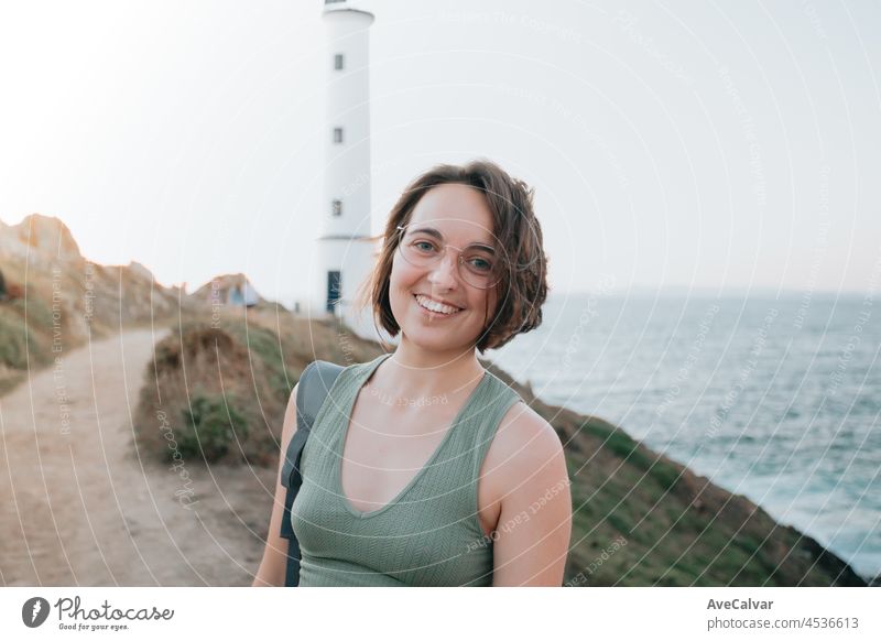 Portrait of a young backpack girl traveler hiker during an stunning sunset coastline scenario, hipster traveler concept, beauty landscape. Movement and liberty, nomad life.