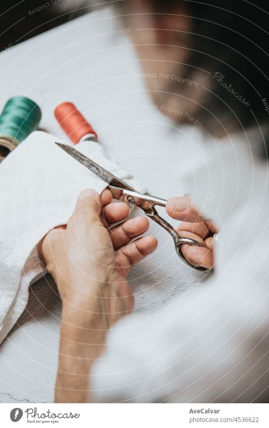 Seamstress old hands sewing and doing works. Cloth working and sewing. Lightful image, copy space, threads of different colors background. Cutting cloth senior